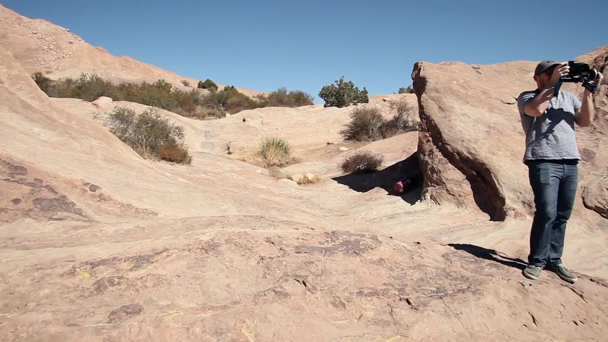 Stylist and photographer discussing red dress against brown rock background