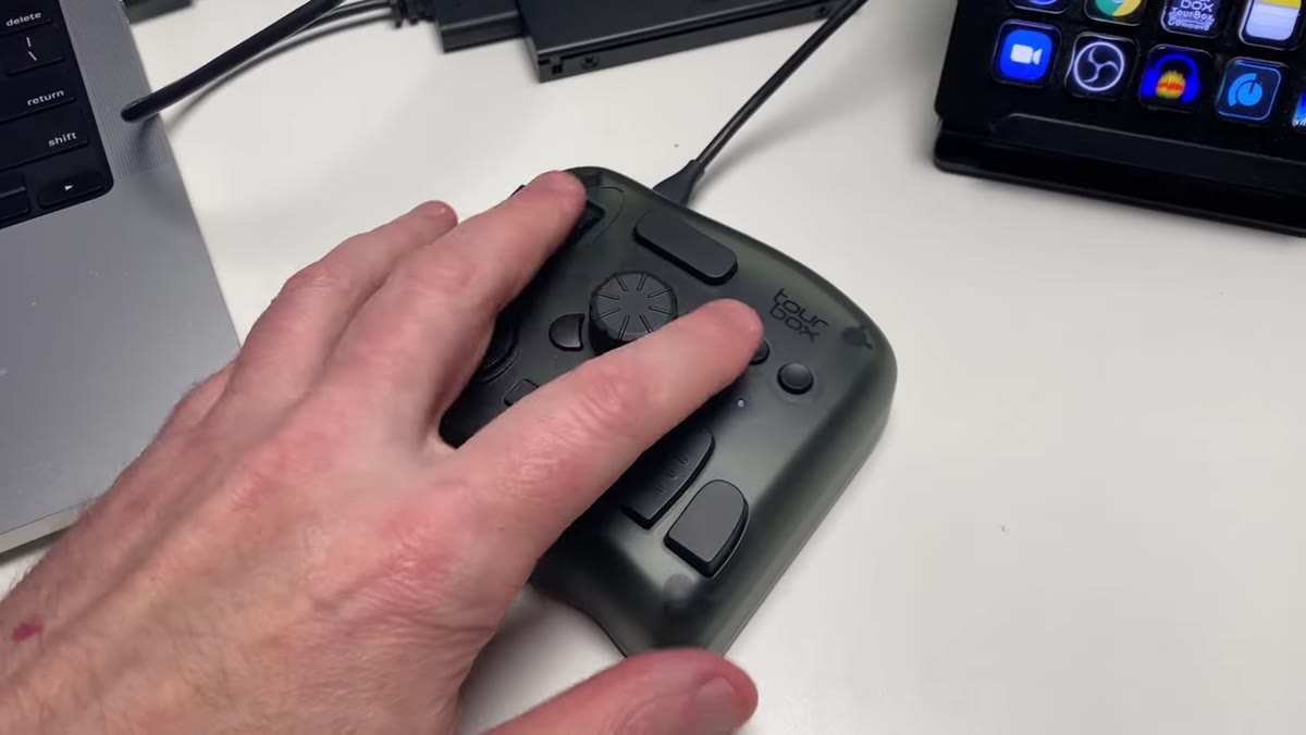 Hand resting naturally on TourBox device, buttons within thumb and finger reach